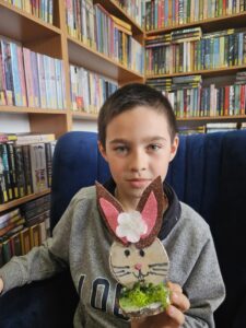 hłopiec trzymający w rękach zajączka, wykonanego własnoręcznie z plastrów drzewa i ozdób.