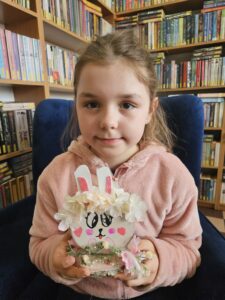 Dziewczynka trzymająca w rękach zajączka, wykonanego własnoręcznie z plastrów drzewa i ozdób.