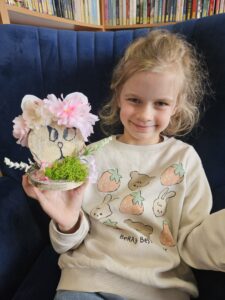 Dziewczynka trzymająca w rękach zajączka, wykonanego własnoręcznie z plastrów drzewa i ozdób.