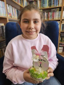 Dziewczynka trzymająca w rękach zajączka, wykonanego własnoręcznie z plastrów drzewa i ozdób.