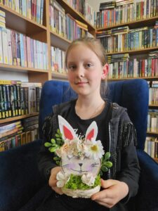 Dziewczynka trzymająca w rękach zajączka, wykonanego własnoręcznie z plastrów drzewa i ozdób.