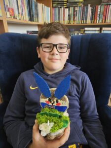 Chłopiec trzymający w rękach zajączka, wykonanego własnoręcznie z plastrów drzewa i ozdób.