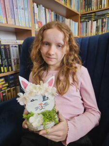 Dziewczynka trzymająca w rękach zajączka, wykonanego własnoręcznie z plastrów drzewa i ozdób.