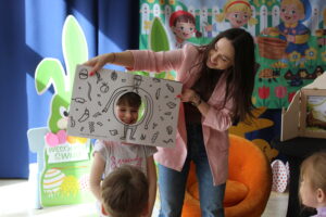 Kobieta z książką z dziurą, w której jest twarz dziecka.