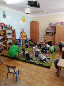 Grupa dzieci i kobieta siedzą na kolorowym dywanie.