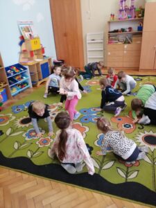 Grupa dzieci siedzących na kolorowym dywanie.