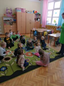 Grupa dzieci siedzących na kolorowym dywanie.