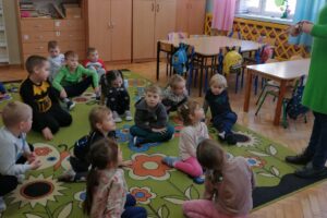 Grupa dzieci siedzących na kolorowym dywanie.