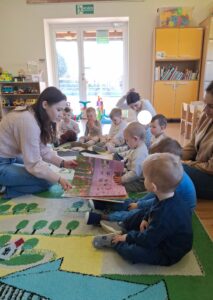 Dzieci i kobieta oglądają wielką książkę, na kolorowym dywanie.