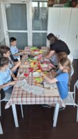 Dzieci i kobieta podczas warsztatów robią kwiaty z bibuły.