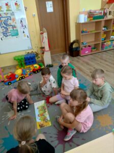 Grupka wesołych dzieci, siedzących na dywanie i przeglądających książkę.