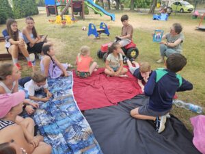 20260630_103826 Kobieta pokazuje książkę dzieciom siedzącym na placu zabaw.