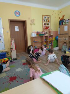 Grupka wesołych dzieci, wykonująca ćwiczenia ruchowe na dywanie.