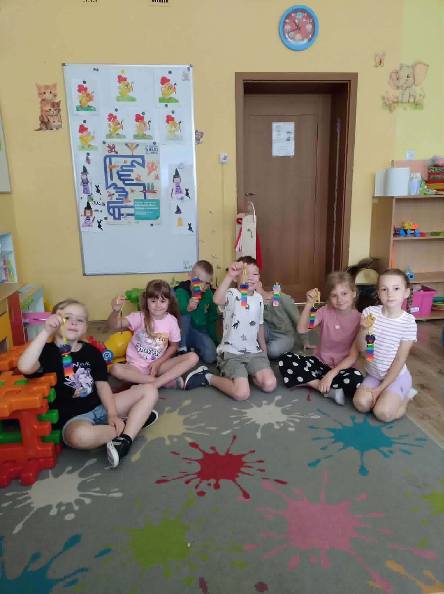 Grupka wesołych dzieci, siedzących na dywanie.