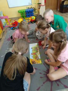 Grupka wesołych dzieci, siedzących na dywanie i przeglądających książkę.