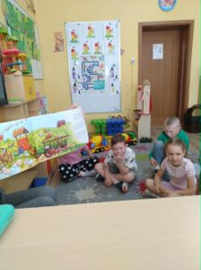 Grupka wesołych dzieci, siedzących na dywanie i oglądających książkę.