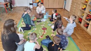 Dzieci i nauczycielki siedzące na dywaniku, oglądają książki.