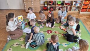 Dzieci i nauczycielki siedzące na dywaniku, oglądają książki.