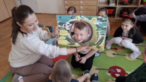 Kobieta trzymająca książkę z dziurą, w której jest twarz dziecka.