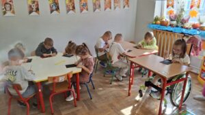 Dzieci w przedszkolu robią wydrapywanki przy stolikach.