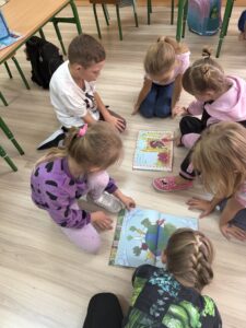 Grupa dzieci czyta książkę,siedząc w kółku na podłodze.