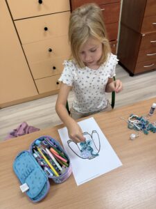 IMG_0139 Dziewczynka wykleja sznureczkami kształt sweterka na kartce.